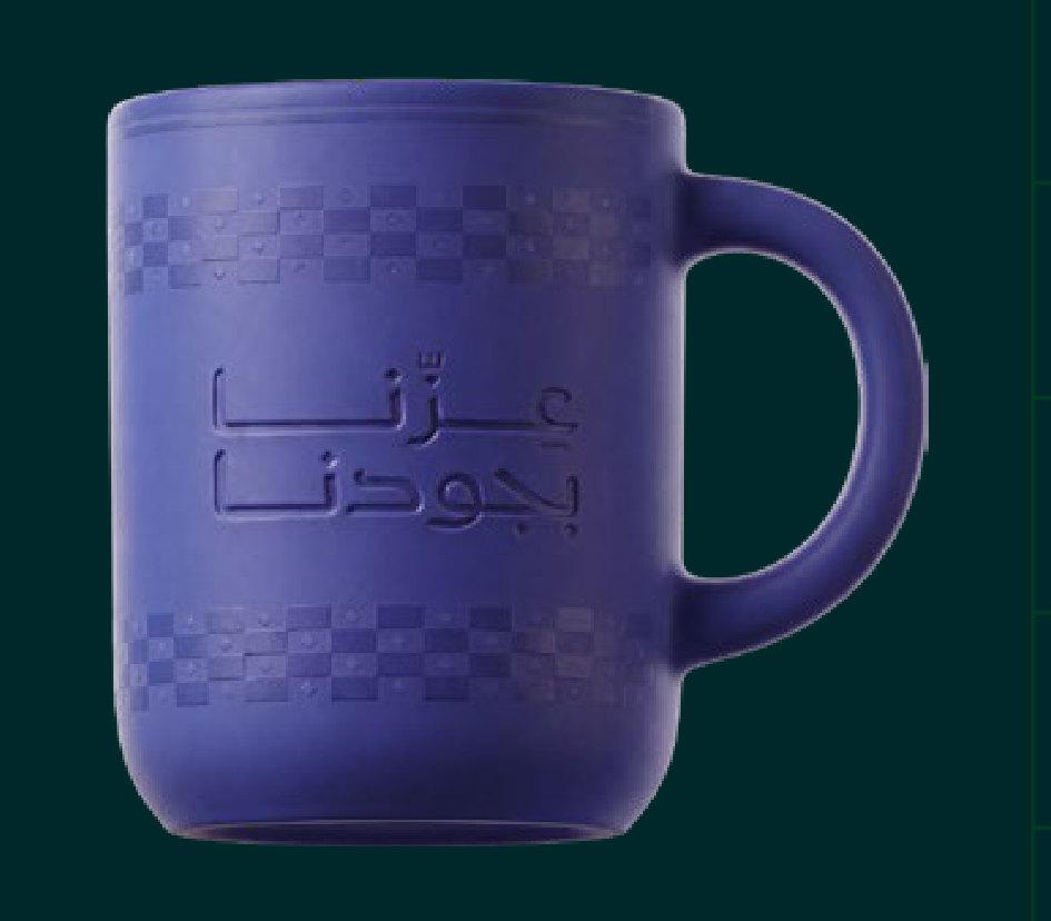 كوب مكتبي بلون بنفسجي يحمل عبارة عزّنا بجودنا
