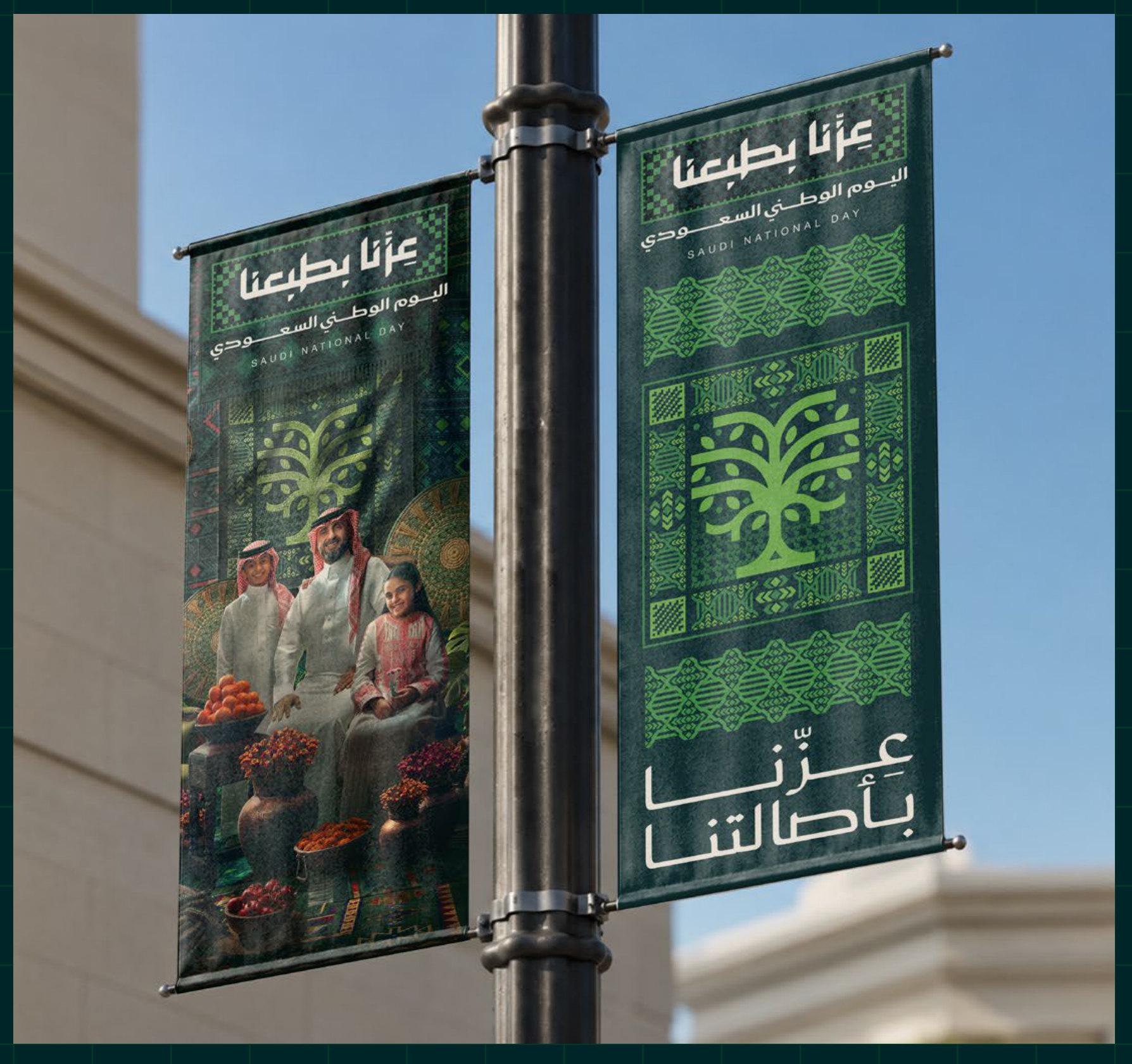 بنرات معلقة على عمود إنارة تحمل تصاميم اليوم الوطني